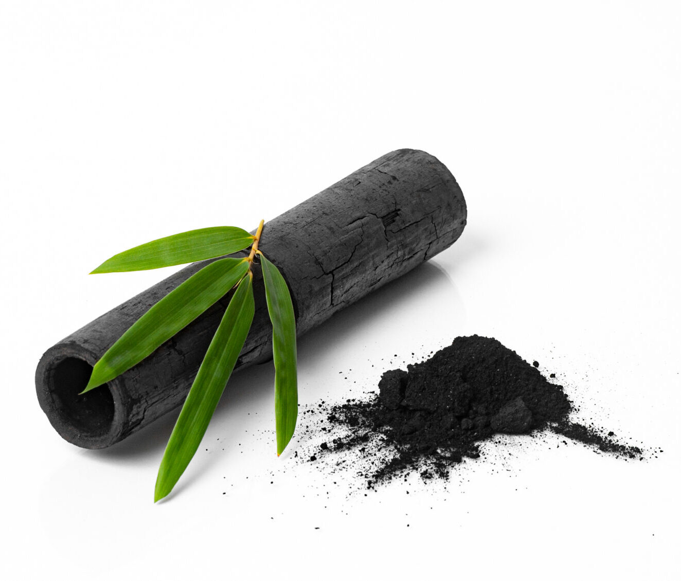 Bamboo charcoal log and powder on a white background with green bamboo leaves