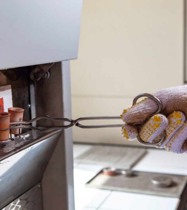 Industrial ceramic crucibles being placed in a furnace with protective gloves